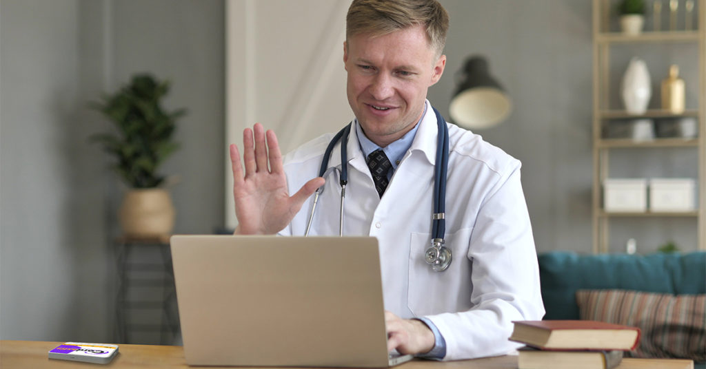 Physician talking to pharma sales rep on video chat using Microsoft Teams with his Swittons remote engagement device next to his laptop working remote.