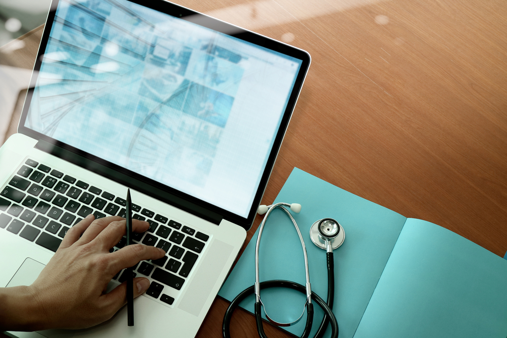 Physician on laptop on a desk while holding a pen.